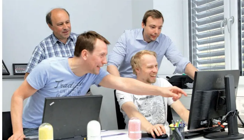 Günter mit Kollegen vor Laptop und Bildschirm im Büro