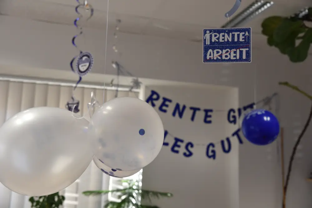 Luftballons und ein „Rente↑ Arbeit↓“-Schild unter der Bürodecke