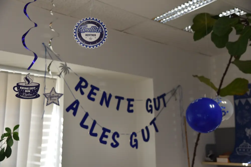Nahaufnahme der „Rente gut, alles gut“-Girlande mit „Endlich Rentner“-Rosette