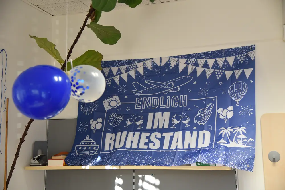 Das große „Endlich im Ruhestand“-Banner über dem Büroregal