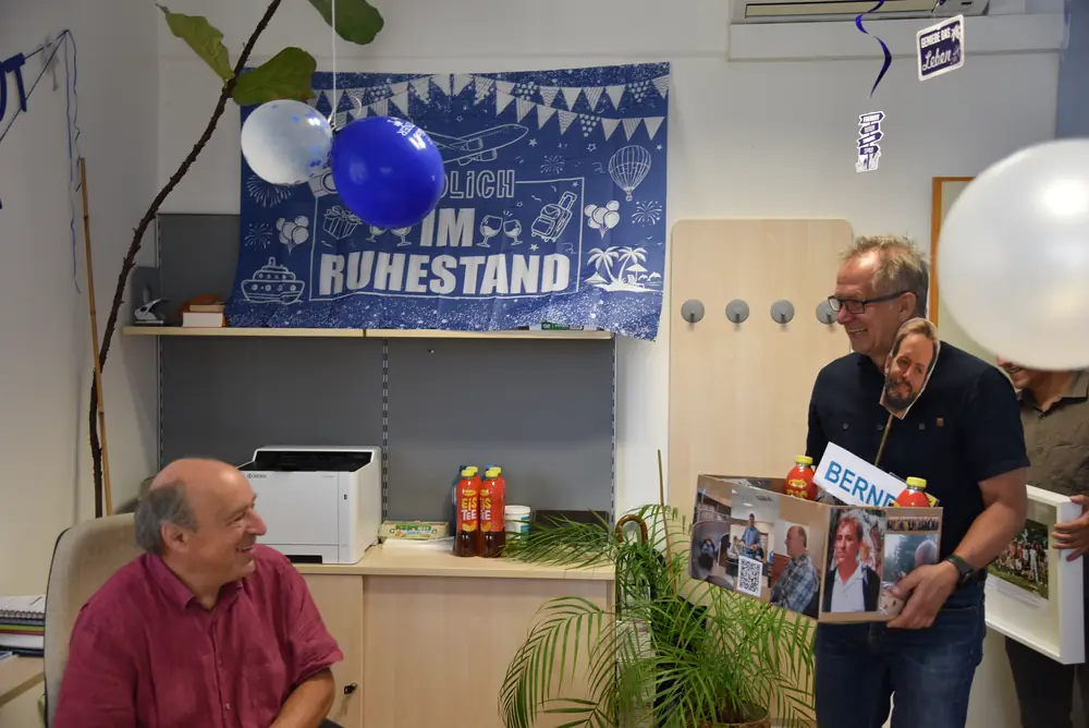 Ein Kollege präsentiert die selbstgebastelte Geschenkkiste, Günter sitzt lachend daneben