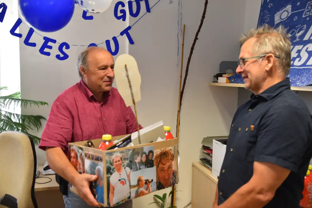 Günter nimmt die Geschenkkiste entgegen, im Gespräch mit einem Kollegen