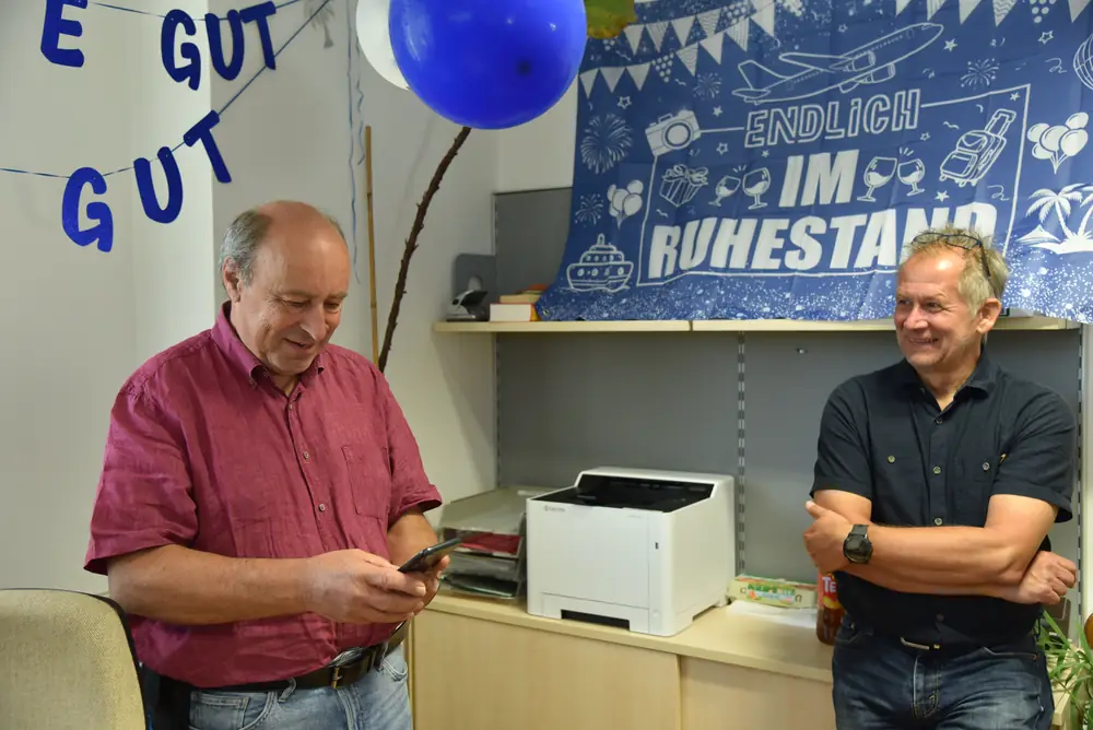 Günter schaut lächelnd auf sein Handy, ein Kollege daneben