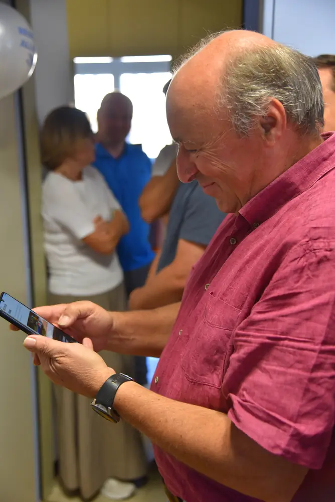Günter mit dem Handy in der Hand, Kolleginnen und Kollegen im Hintergrund