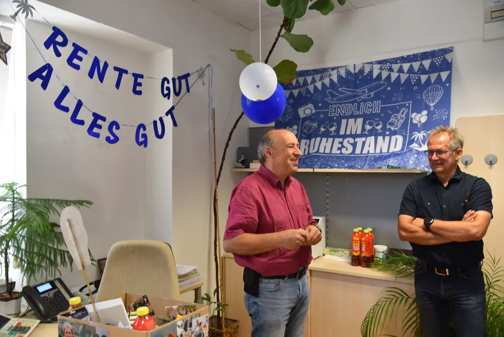 Günter und ein Kollege lachen gemeinsam vor dem Ruhestand-Banner